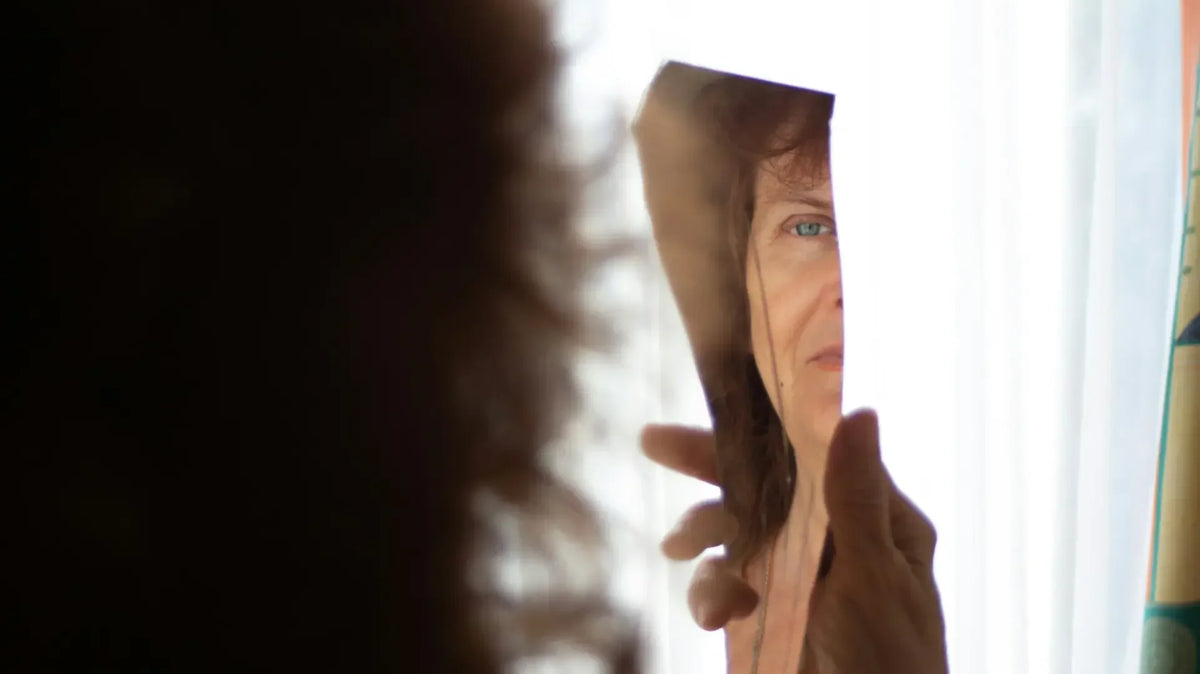 Woman looking at her reflection in a broken mirror, reflecting feelings of low self-esteem — photo by Anita Jankovic