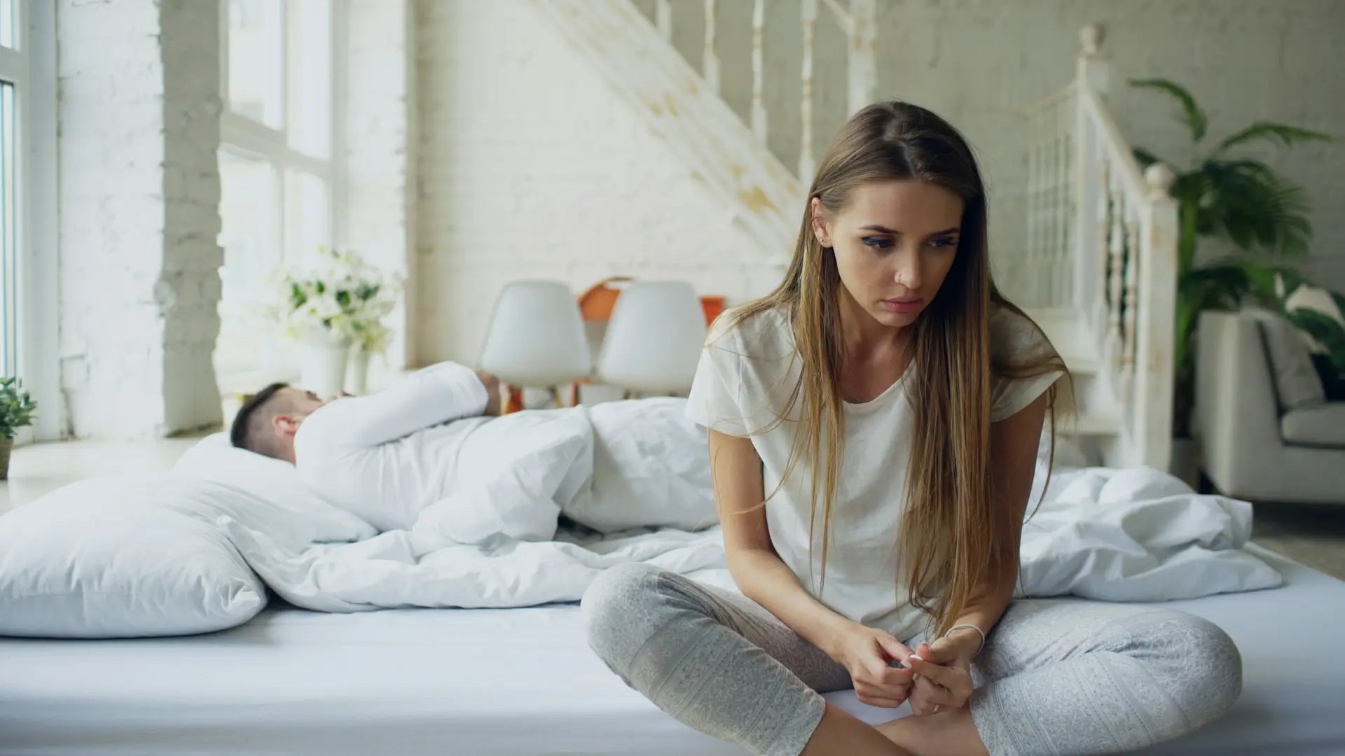 Woman sitting apart from her partner in bed, reflecting the strain sexual problems can cause in a relationship — photo by Vitaly Gariev