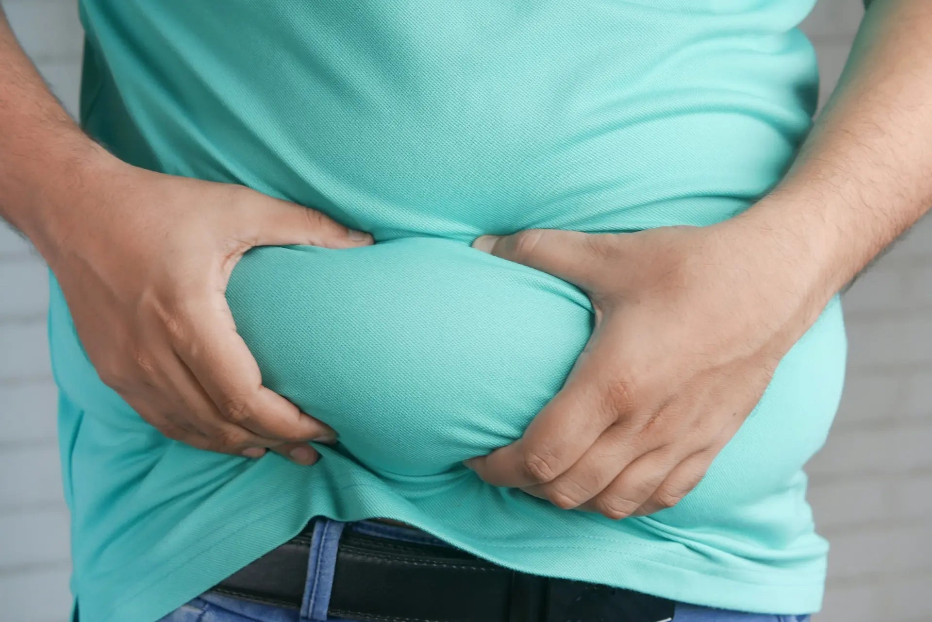 Man pinching belly fat, reflecting a symptom linked to high oestrogen levels — photo by Towfiqu Barbhuiya